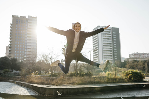 Glückliche junge Frau springt in einem Park mit der Stadt im Hintergrund, lizenzfreies Stockfoto