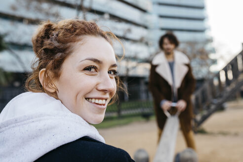 Porträt einer glücklichen jungen Frau mit ihrem Freund auf einer Wippe auf einem Spielplatz - JRFF02699
