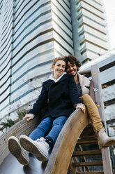 Portrait of happy couple on a slide at a playground in the city - JRFF02701