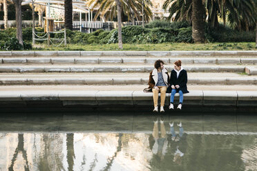 Paar sitzt in einem Park am Wasser und unterhält sich - JRFF02702
