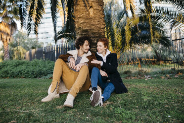 Couple sitting in the park leaning against a palm tree - JRFF02710