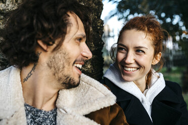 Porträt eines glücklichen Paares an einem Baumstamm im Park - JRFF02712