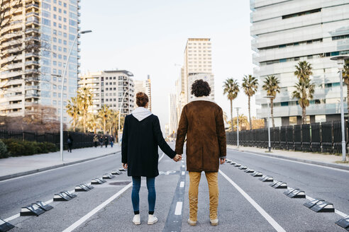 Rear view of a couple holding hands in the middle of the street looking at the buildings in the background - JRFF02714