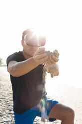 Mann mit VR-Brille am Strand, der Sand durch seine Hände rieseln lässt - HMEF00222