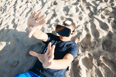 Mann mit VR-Brille liegt im Sand am Strand - HMEF00225