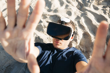 Mann mit VR-Brille liegt im Sand am Strand - HMEF00226