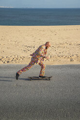 Spain, Tarifa, man wearing colourful suit skateboarding on road - KBF00514