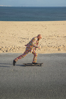 Spain, Tarifa, man wearing colourful suit skateboarding on road - KBF00514