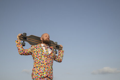 Bearded man with longboard on his shoulders wearing suit with colourful polka-dots - KBF00516