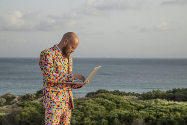 Man wearing suit with colourful polka-dots using laptop outdoors - KBF00521