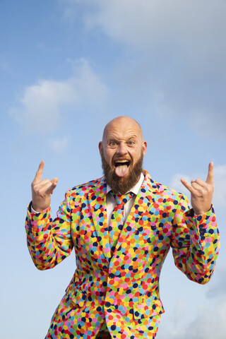 Portrait of bald man with beard wearing suit with colourful polka-dots sticking out tongue stock photo