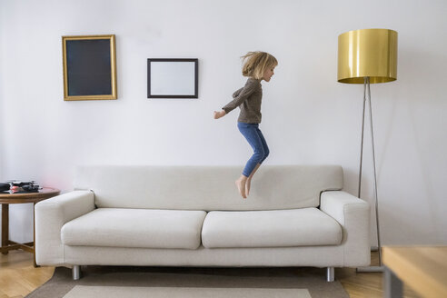 Little girl jumping in the air on the couch at home - PSIF00242