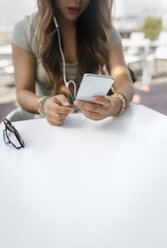 Smartphone in der Hand einer Frau in einem Straßencafé, Teilansicht - MGOF03942