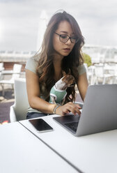 Porträt einer Frau in einem Straßencafé, die mit ihrem Chihuahua-Hündchen auf dem Schoß am Laptop arbeitet - MGOF03945