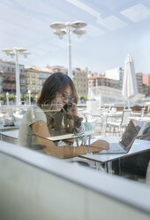 Lachende Frau am Telefon in einem Straßencafé mit ihrem Chihuahua-Welpen - MGOF03951