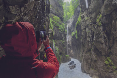 Deutschland, Bayern, Partnachschlucht bei Garmisch-Partenkirchen, Mann mit roter Regenjacke beim Fotografieren mit Smarthone - MMAF00828