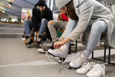 Freunde beim Anziehen von Schlittschuhen auf einer Eisbahn - ZEDF01873