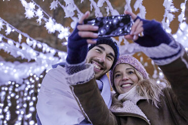 Glückliches junges Paar in Winterdekoration nimmt ein Selfie - ZEDF01878