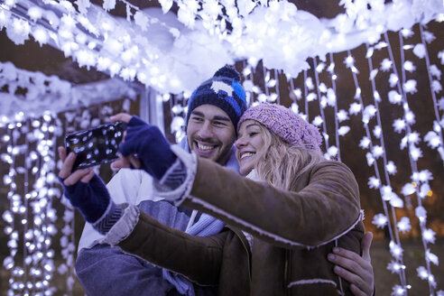Glückliches junges Paar in Winterdekoration nimmt ein Selfie - ZEDF01879