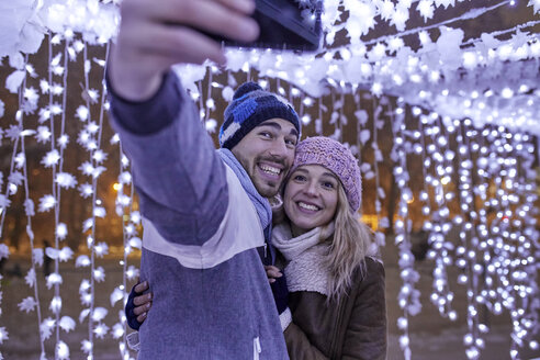 Glückliches junges Paar in Winterdekoration nimmt ein Selfie - ZEDF01880