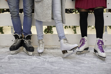 Legs of friends wearing ice skates standing at an ice rink - ZEDF01882