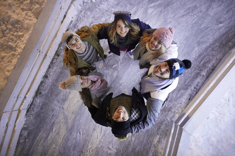 Glückliche Freunde, die sich nachts auf einer Eisbahn zusammenkauern, lizenzfreies Stockfoto