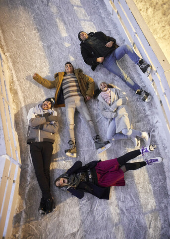 Glückliche Freunde liegen nachts auf einer Eisbahn, lizenzfreies Stockfoto