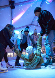 Glückliche Freunde beim Schlittschuhlaufen auf einer Eisbahn, die einem Mann beim Aufstehen helfen - ZEDF01888