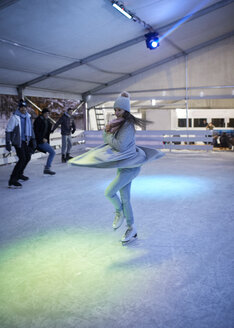 Junge Frau dreht eine Pirouette auf einer nächtlichen Eisbahn, beobachtet von ihren Freunden - ZEDF01889