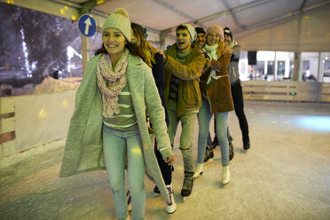 Happy friends ice skating on an ice rink at night - ZEDF01890