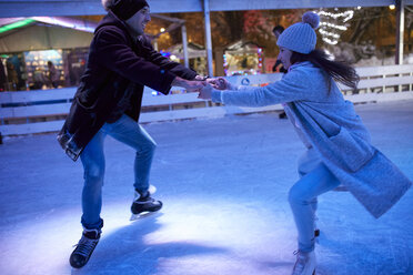 Happy young couple ice skating on an ice rink at night - ZEDF01891