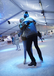 Glückliches junges Paar, das sich nachts auf einer Eislaufbahn umarmt - ZEDF01892