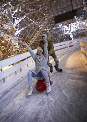 Glückliches verspieltes Paar beim Schlittschuhlaufen auf einer Eisbahn - ZEDF01895
