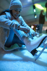 Frau sitzt auf einer Eisbahn und zieht Schlittschuhe an - ZEDF01898