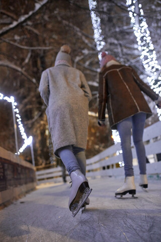 Rückansicht von Freunden beim Schlittschuhlaufen auf einer Eisbahn bei Nacht, lizenzfreies Stockfoto