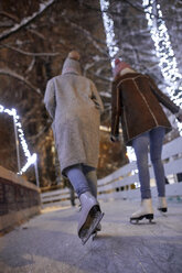 Rückansicht von Freunden beim Schlittschuhlaufen auf einer Eisbahn bei Nacht - ZEDF01901