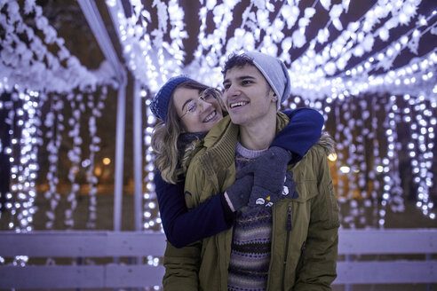 Glückliches junges Paar, das sich in der Winterdekoration umarmt - ZEDF01904