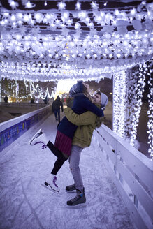 Glückliches junges Paar, das sich nachts auf einer Eislaufbahn umarmt - ZEDF01913
