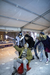 Glückliche verspielte Freunde mit einer Kamera beim Schlittschuhlaufen auf einer Eisbahn - ZEDF01918