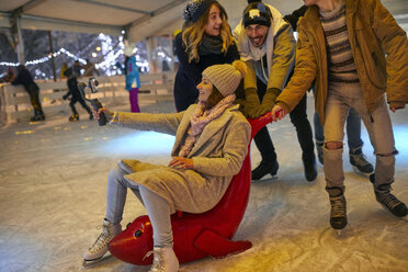 Glückliche verspielte Freunde mit einer Kamera beim Schlittschuhlaufen auf einer Eisbahn - ZEDF01921