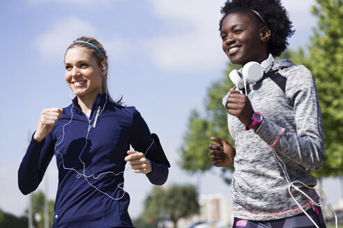 Two happy sporty young women running together in the city - JSRF00117