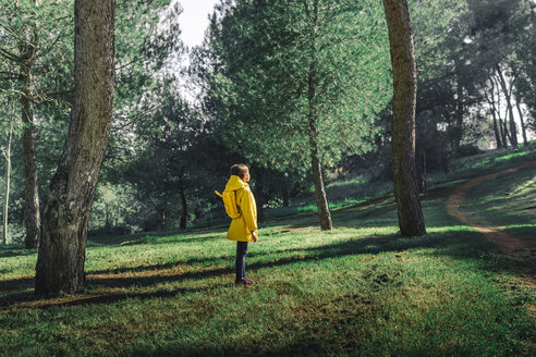 Mädchen mit gelbem Regenmantel und gelbem Rucksack steht auf einer Wiese - ERRF00770