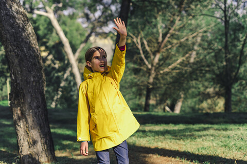 Mädchen in gelbem Regenmantel steht im Sonnenlicht und schützt die Augen mit der Hand, lizenzfreies Stockfoto