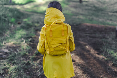 Rückenansicht eines Mädchens mit gelbem Regenmantel und gelbem Rucksack in der Natur, lizenzfreies Stockfoto