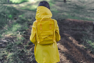 Back view of girl wearing yellow raincoat and yellow backpack in nature - ERRF00775