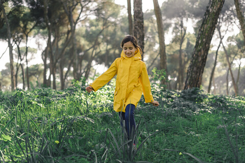 Lächelndes Mädchen mit gelbem Regenmantel und Spaziergang im Wald, lizenzfreies Stockfoto