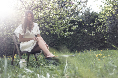 Junge Frau in weißem Kleid, die im Garten sitzt und ein Fußbad nimmt, lizenzfreies Stockfoto