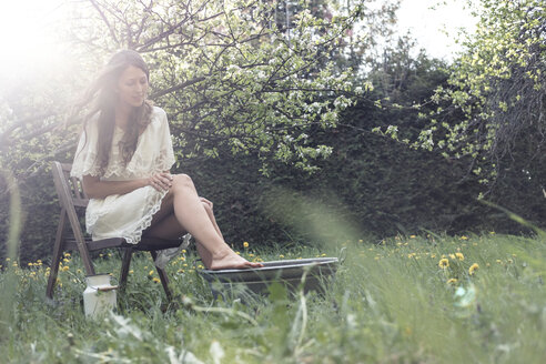 Young woman wearing white dress sittiing in garden taking footbath - WFF00013