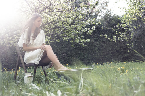 Junge Frau in weißem Kleid, die im Garten sitzt und ein Fußbad nimmt - WFF00014