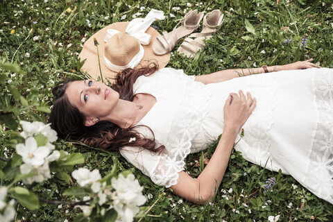 Porträt einer träumenden jungen Frau in weißem Spitzenkleid auf einer Blumenwiese liegend, lizenzfreies Stockfoto